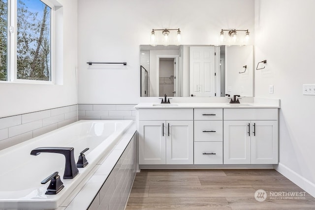 bathroom featuring a relaxing tiled tub, hardwood / wood-style flooring, and vanity