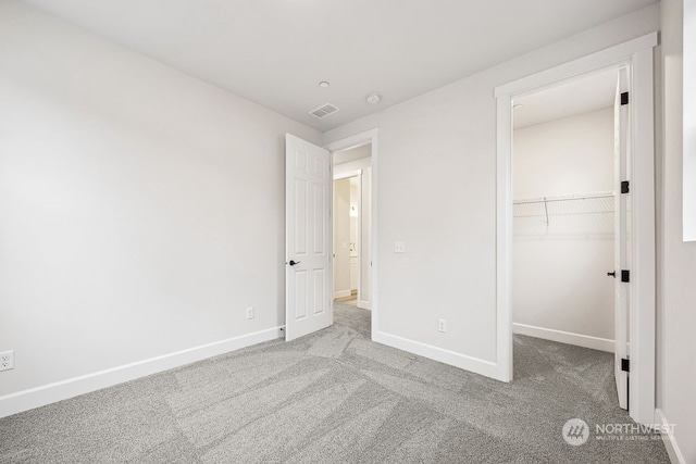 unfurnished bedroom featuring a spacious closet, a closet, and light colored carpet