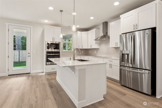 kitchen with appliances with stainless steel finishes, wall chimney exhaust hood, decorative light fixtures, white cabinetry, and sink