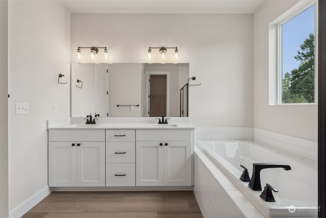 bathroom with hardwood / wood-style floors, a relaxing tiled tub, plenty of natural light, and vanity