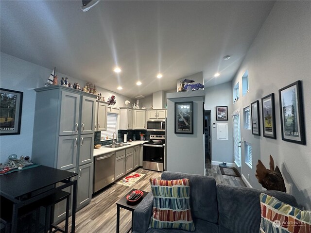 kitchen with light wood-type flooring, tasteful backsplash, stainless steel appliances, sink, and gray cabinets