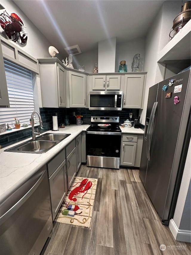 kitchen featuring appliances with stainless steel finishes, tasteful backsplash, gray cabinetry, sink, and dark hardwood / wood-style floors