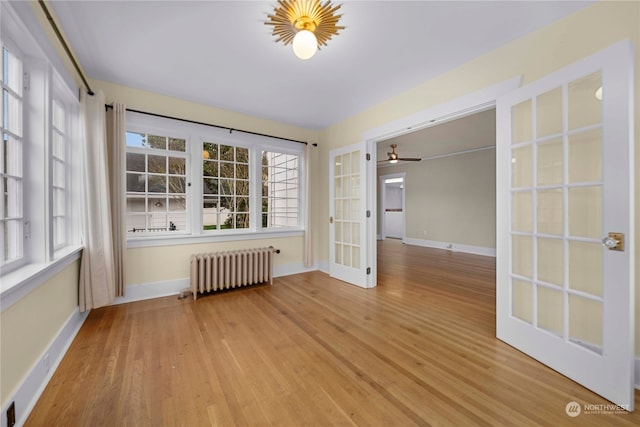 empty room with light hardwood / wood-style floors, ceiling fan, radiator heating unit, and french doors