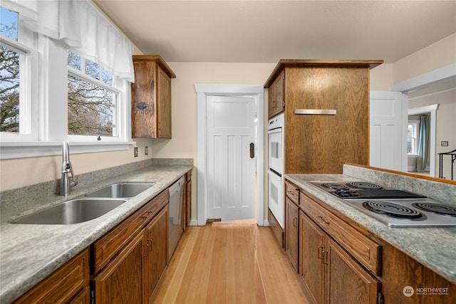 kitchen with white double oven, dishwasher, cooktop, light hardwood / wood-style flooring, and sink