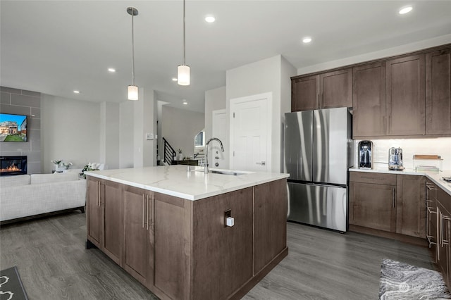 kitchen with a center island with sink, sink, dark hardwood / wood-style floors, stainless steel fridge, and decorative light fixtures