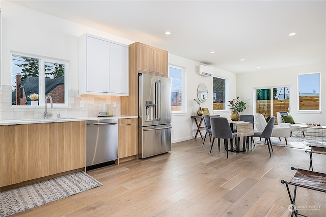 kitchen with light wood-type flooring, stainless steel appliances, a healthy amount of sunlight, sink, and white cabinetry