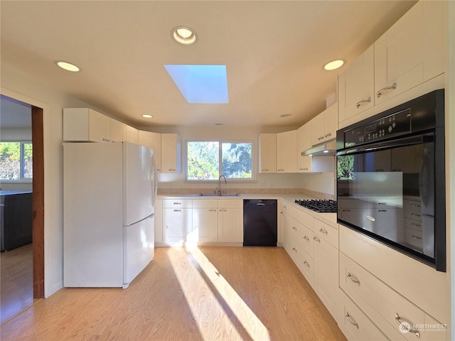 kitchen featuring light hardwood / wood-style flooring, black appliances, a skylight, sink, and white cabinetry