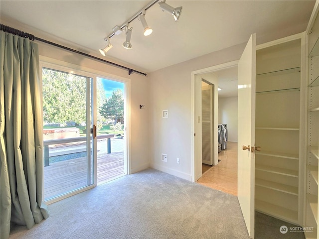 empty room featuring track lighting, washing machine and dryer, and light colored carpet