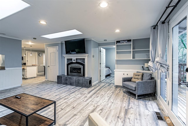 living room with a skylight, crown molding, a tiled fireplace, and light wood-type flooring