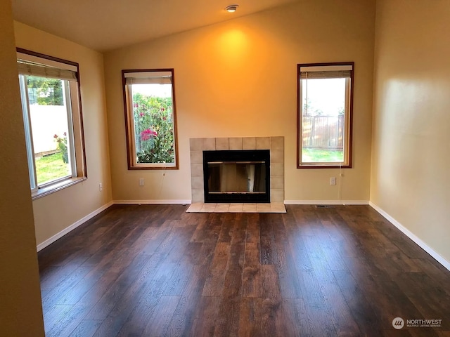 unfurnished living room featuring a tiled fireplace, vaulted ceiling, and dark hardwood / wood-style floors