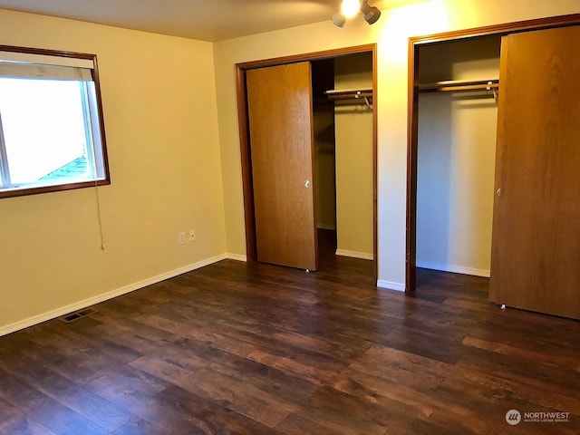 unfurnished bedroom featuring dark hardwood / wood-style floors and multiple closets