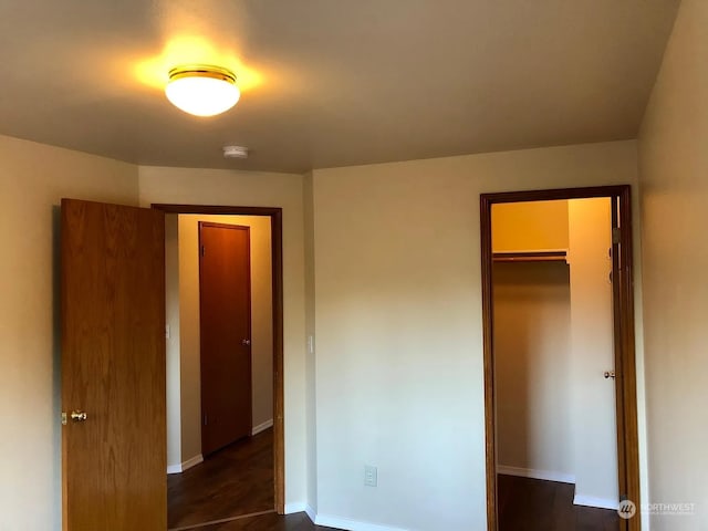 unfurnished bedroom featuring dark wood-type flooring, a spacious closet, and a closet