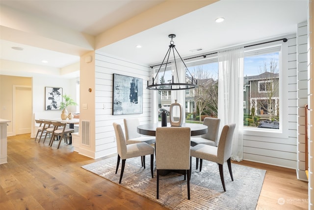 dining area with wooden walls, light hardwood / wood-style floors, and a notable chandelier