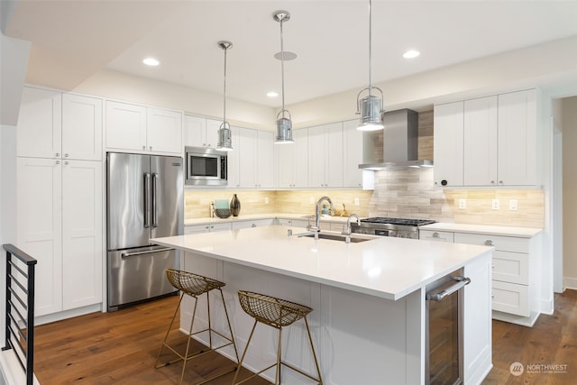 kitchen featuring built in appliances, white cabinetry, hanging light fixtures, and wall chimney exhaust hood