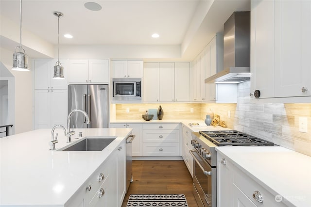 kitchen featuring high quality appliances, white cabinets, wall chimney range hood, sink, and hanging light fixtures