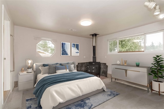 bedroom with a wood stove, light carpet, and visible vents