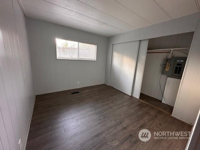 unfurnished bedroom featuring dark hardwood / wood-style floors, wooden walls, and a closet