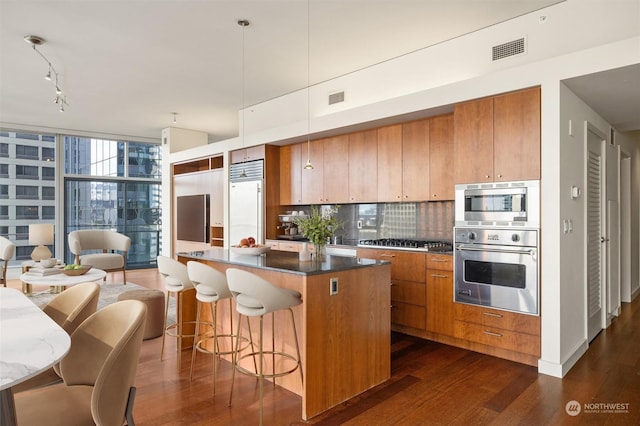 kitchen featuring stainless steel appliances, dark wood-type flooring, hanging light fixtures, tasteful backsplash, and a wall of windows