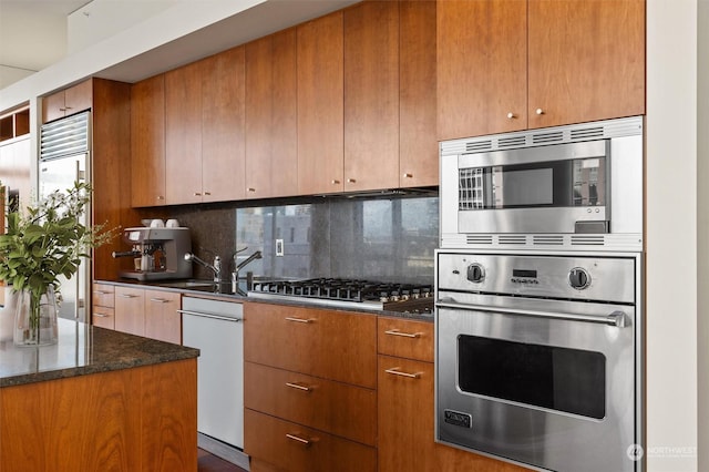 kitchen featuring tasteful backsplash, built in appliances, dark stone countertops, and sink