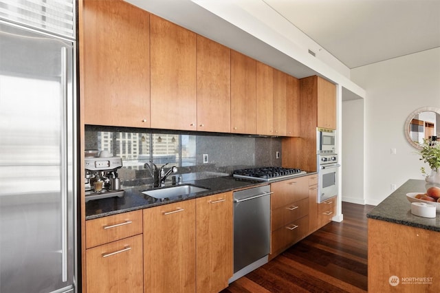 kitchen featuring built in appliances, dark hardwood / wood-style floors, dark stone countertops, and sink