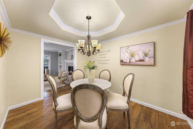 dining area with dark wood-type flooring, an inviting chandelier, crown molding, and a tray ceiling