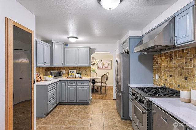 kitchen featuring stainless steel appliances, gray cabinetry, wall chimney range hood, and tasteful backsplash