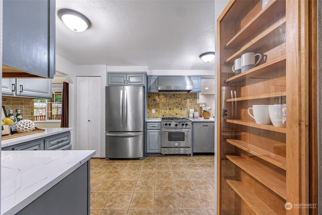 kitchen featuring light stone counters, wall chimney exhaust hood, stainless steel appliances, tasteful backsplash, and gray cabinetry