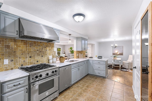 kitchen with gray cabinets, stainless steel appliances, kitchen peninsula, ventilation hood, and decorative light fixtures