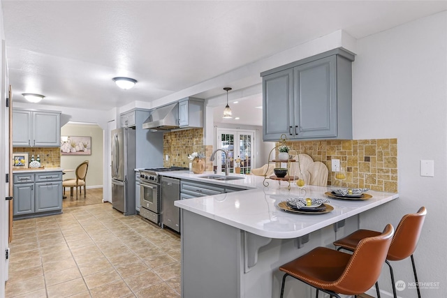 kitchen featuring kitchen peninsula, pendant lighting, stainless steel appliances, tasteful backsplash, and sink