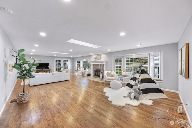 living room featuring french doors, a skylight, a brick fireplace, and wood-type flooring