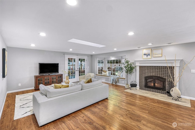 living room with wood-type flooring, a tile fireplace, a skylight, and french doors