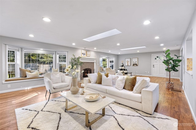 living room featuring a fireplace, a skylight, a healthy amount of sunlight, and light hardwood / wood-style flooring