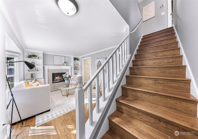 stairs with ornamental molding, hardwood / wood-style floors, built in shelves, and a fireplace