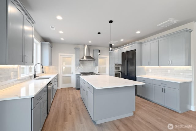 kitchen featuring wall chimney range hood, gray cabinets, a sink, and appliances with stainless steel finishes