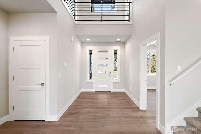 foyer with stairway, a towering ceiling, baseboards, and wood finished floors