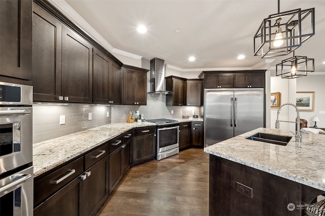 kitchen with sink, hanging light fixtures, stainless steel appliances, wall chimney range hood, and ornamental molding