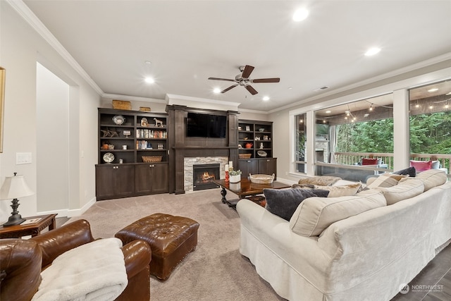 living room with a stone fireplace, ceiling fan, carpet floors, and ornamental molding