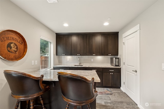 kitchen with hardwood / wood-style floors, kitchen peninsula, light stone counters, dark brown cabinetry, and a breakfast bar area