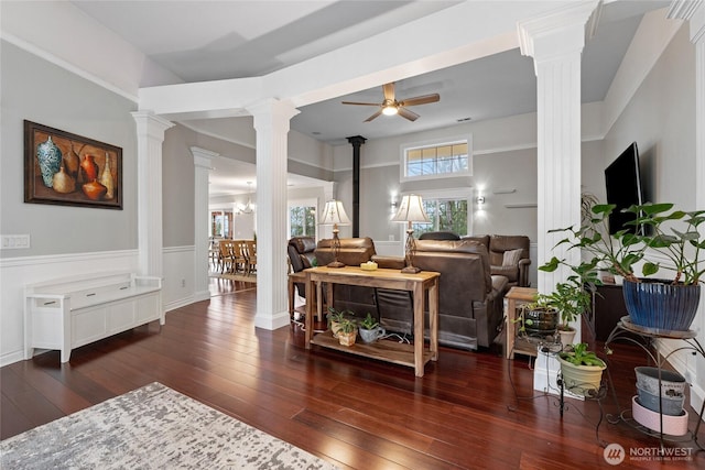 living area featuring a wood stove, ornate columns, a ceiling fan, and hardwood / wood-style floors