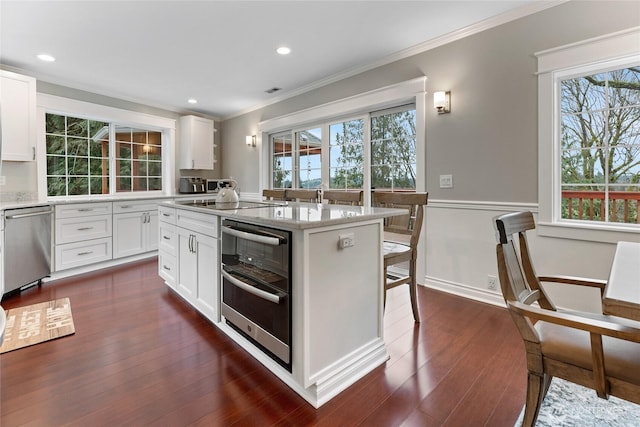 kitchen with light stone counters, dark wood-style floors, stainless steel dishwasher, ornamental molding, and a kitchen island with sink