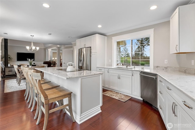 kitchen featuring stainless steel appliances, dark wood-style flooring, a sink, open floor plan, and decorative columns