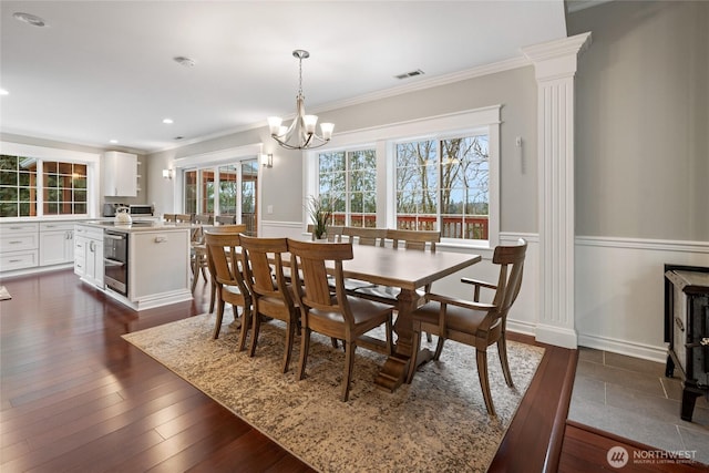 dining space featuring a wainscoted wall, dark wood-type flooring, an inviting chandelier, and crown molding