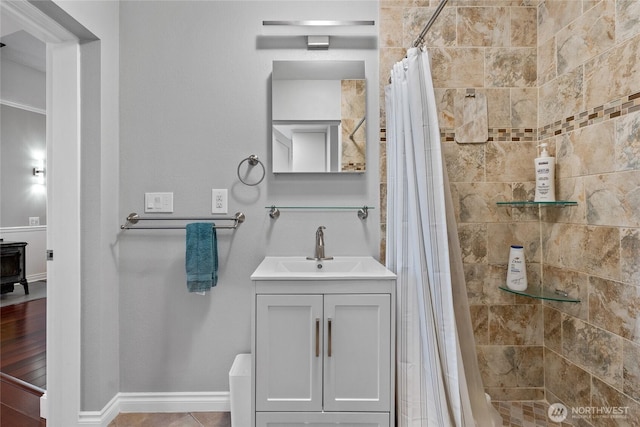 bathroom featuring a wood stove, baseboards, a tile shower, and vanity