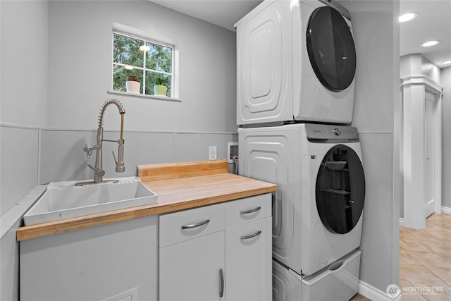 laundry room featuring recessed lighting, cabinet space, stacked washer / dryer, light tile patterned flooring, and a sink