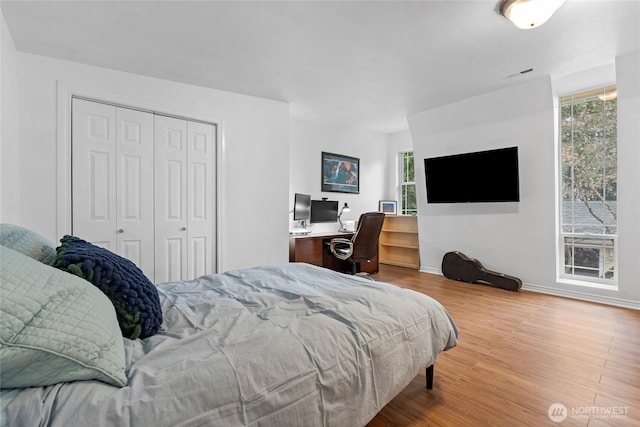 bedroom with a closet, wood finished floors, visible vents, and baseboards