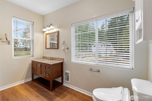 half bathroom featuring baseboards, vanity, toilet, and wood finished floors