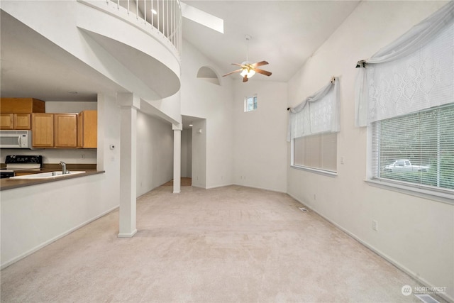 unfurnished living room featuring a healthy amount of sunlight, ceiling fan, high vaulted ceiling, and light colored carpet