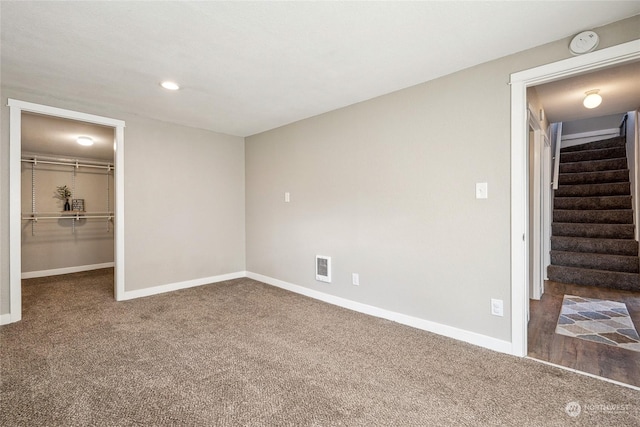 unfurnished bedroom featuring dark carpet, a walk in closet, and a closet