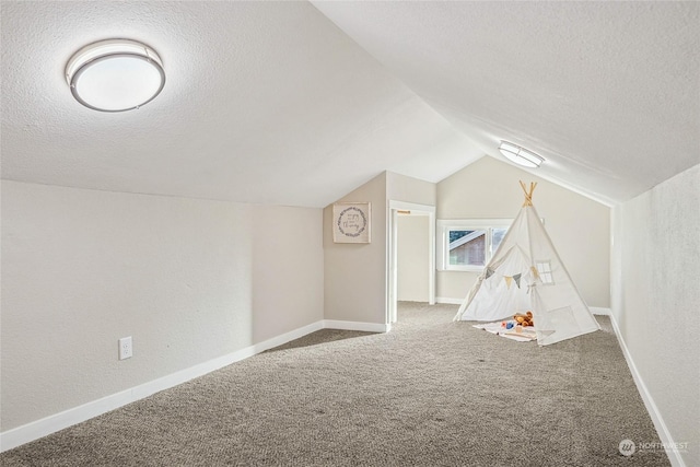 recreation room with a textured ceiling, carpet floors, and vaulted ceiling