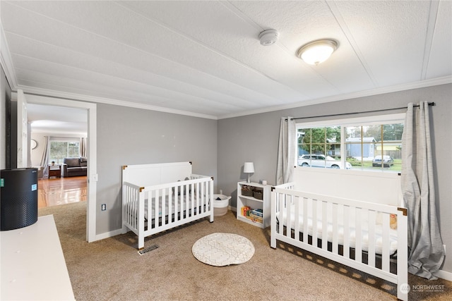 bedroom with carpet flooring, a crib, ornamental molding, and a textured ceiling